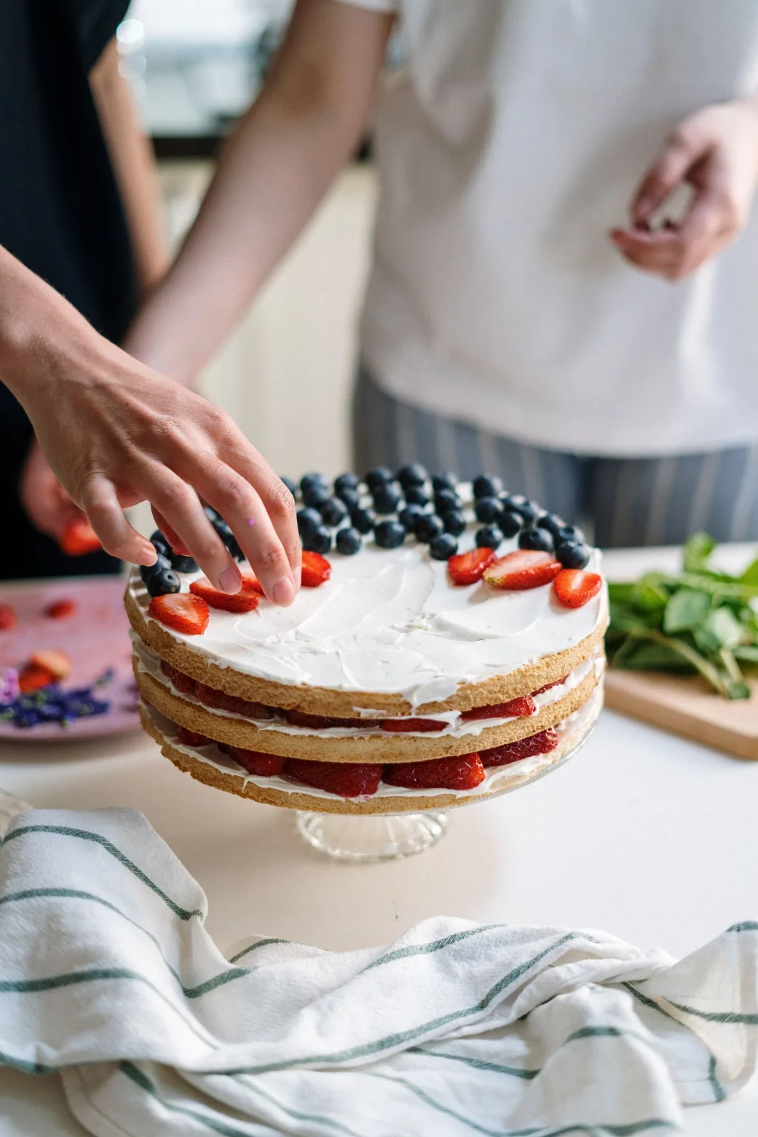 Hands decorating a berry-topped cake